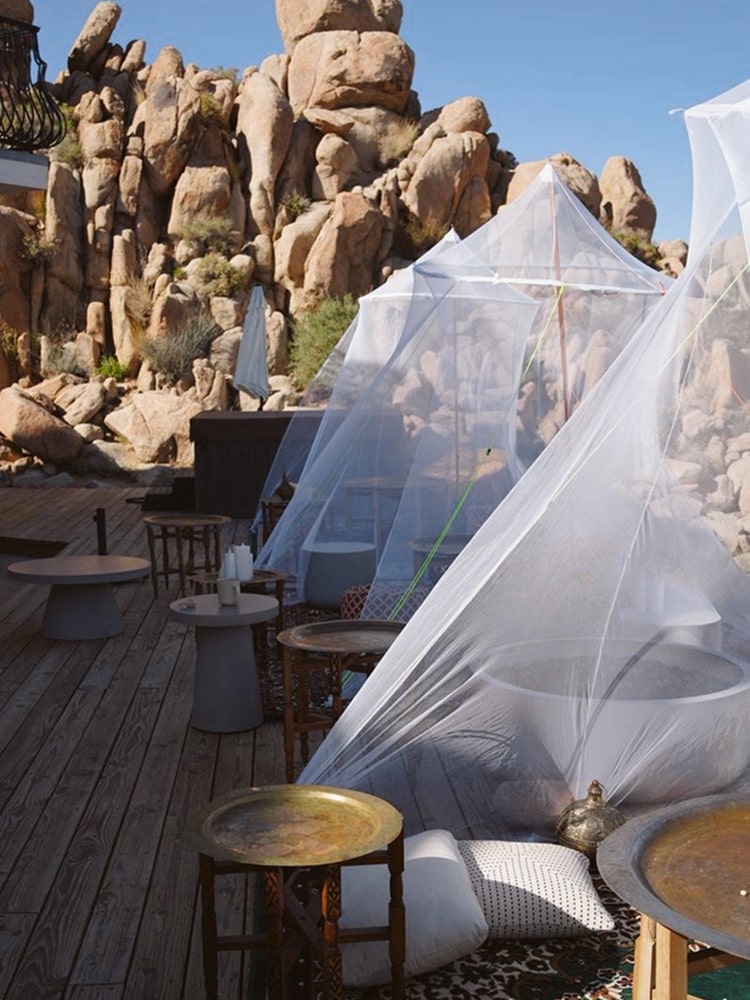 White canopies, low tables and cushions on a wooden deck among desert boulders