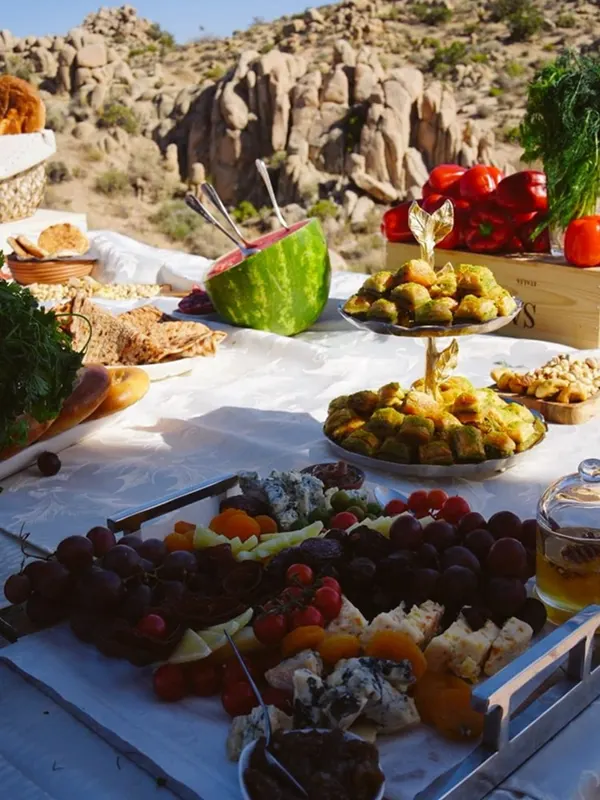 A grazing table with watermelon, cheeses, grapes and pastries set up among desert rocks