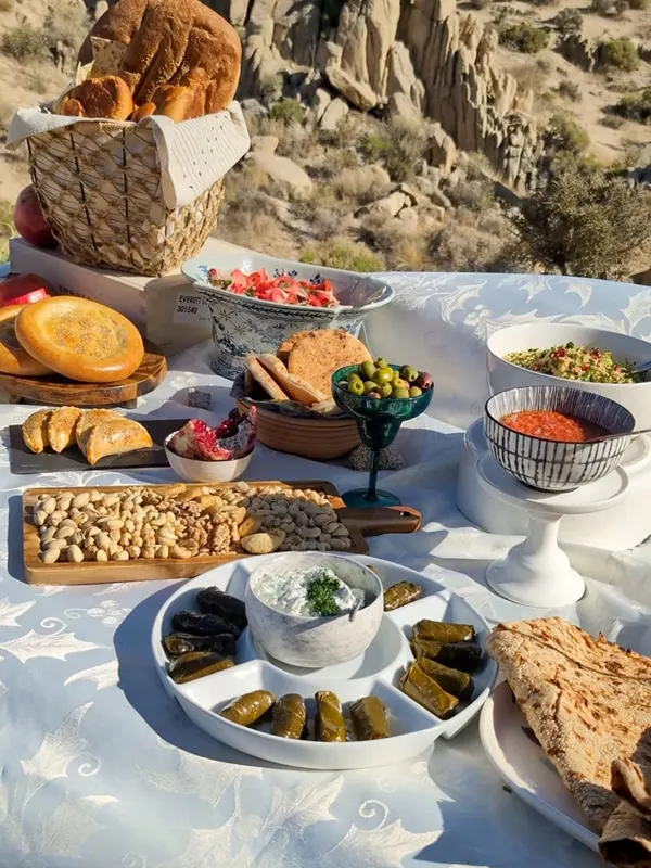 A desert picnic of bread, dips, stuffed grape leaves and pistachios on a white cloth among boulders