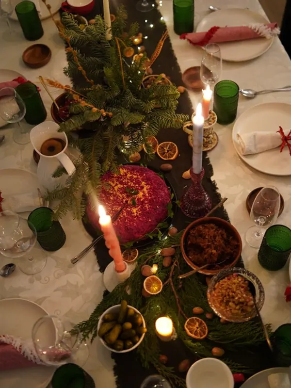 Overhead view of a holiday table with evergreen garland, dried oranges, green glassware and lit candles