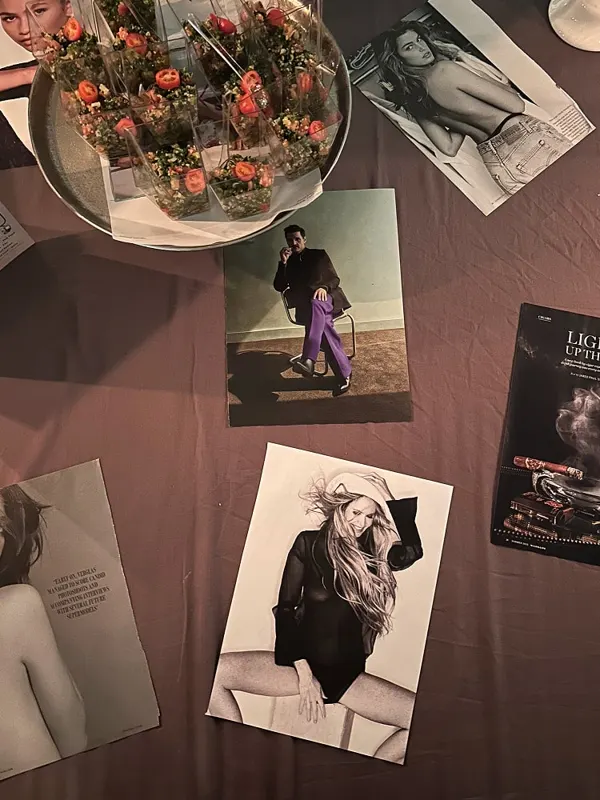 Overhead view of fashion photographs and magazines arranged on a dark tablecloth around a bowl of roses