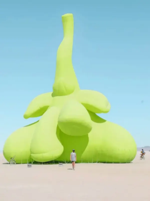 A giant lime-green inflatable sculpture standing in the desert under a blue sky