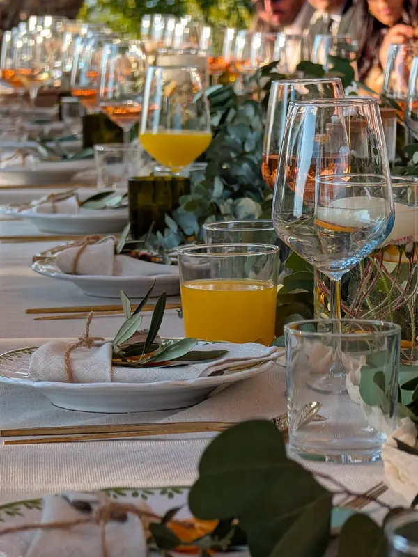 Close-up of a long table set with wine glasses, orange juice, linen napkins and greenery