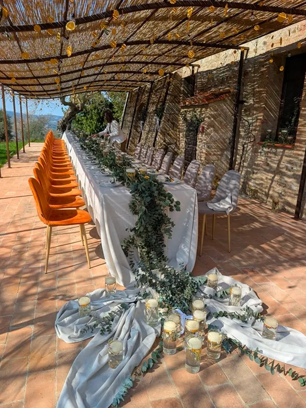 A long table with orange chairs and cascading greenery under a reed pergola