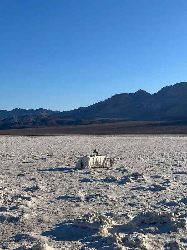 A lone dinner table on a white salt flat with mountains in the distance