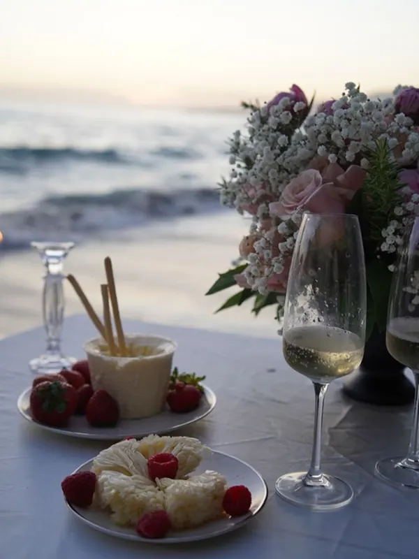 Strawberries, dessert and champagne on a seaside table at dusk beside a pink and white bouquet