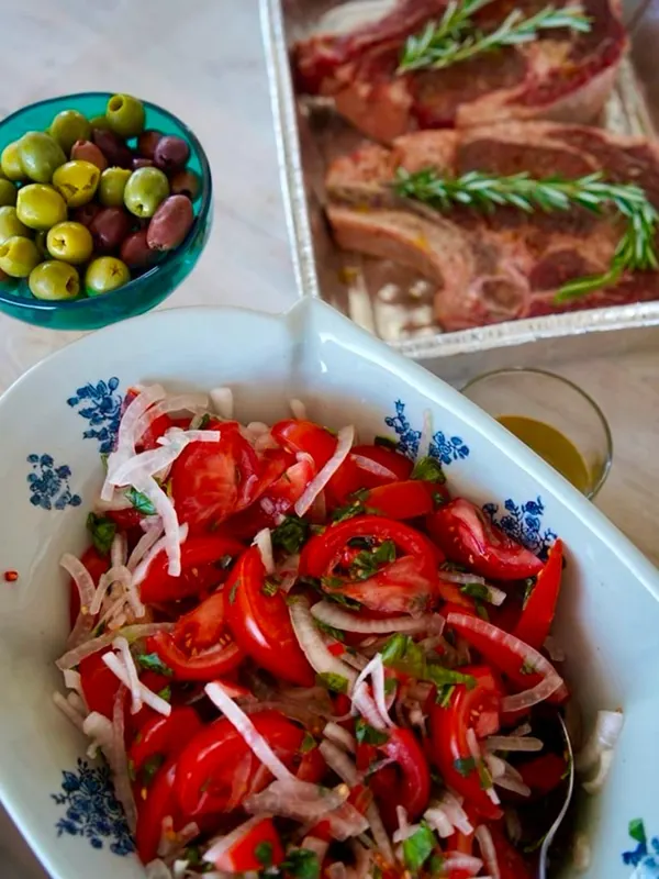 A tomato and onion salad in a blue-and-white dish with olives and grilled meat