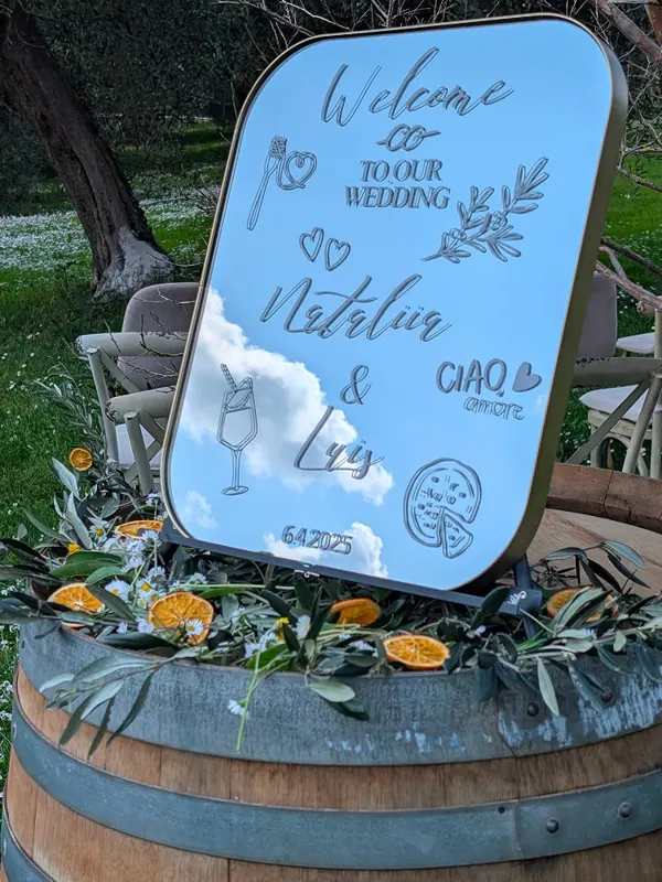 A mirrored wedding welcome sign on a wine barrel decorated with olive branches and dried orange slices