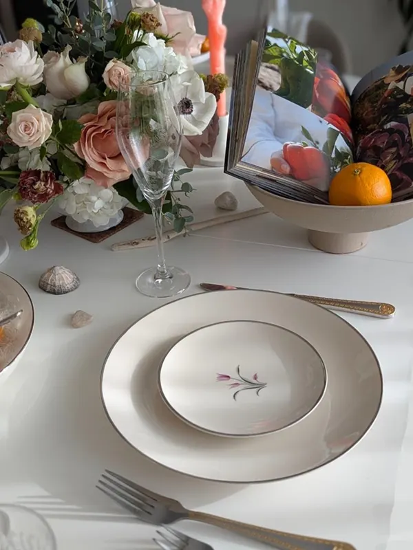 A white place setting with a floral plate, crystal glass and a fresh flower arrangement