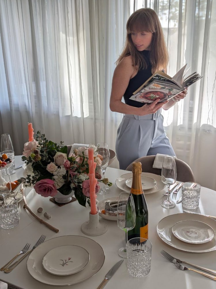 Katia Kado, founder of Zest & Zorya, beside a dinner table set with pink taper candles, roses and champagne