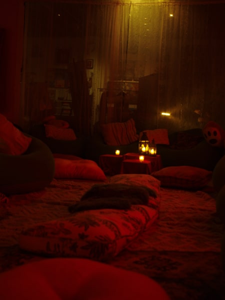 A candlelit lounge with floor cushions and low tables bathed in deep red light