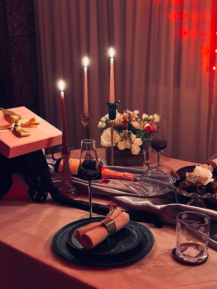A red-toned tablescape with tall taper candles, dark plates, copper napkins and garden roses